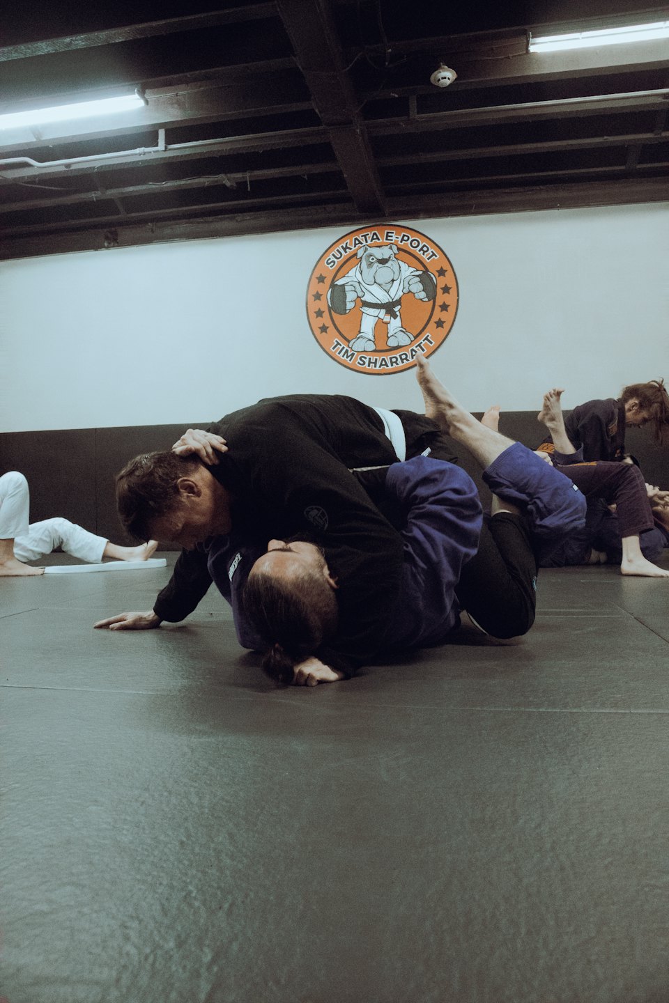 Dos practicantes luchan sobre una esterilla en un estudio de artes marciales.